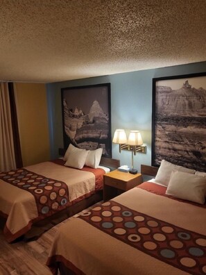A hotel room with two beds, each with a patterned bedspread, a nightstand with a lamp, and two framed pictures on the wall.
