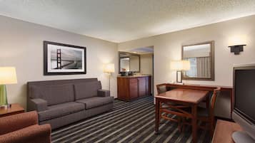Habitación de hotel con sofá, mesa de comedor, televisión, espejo y un cuadro de un puente.