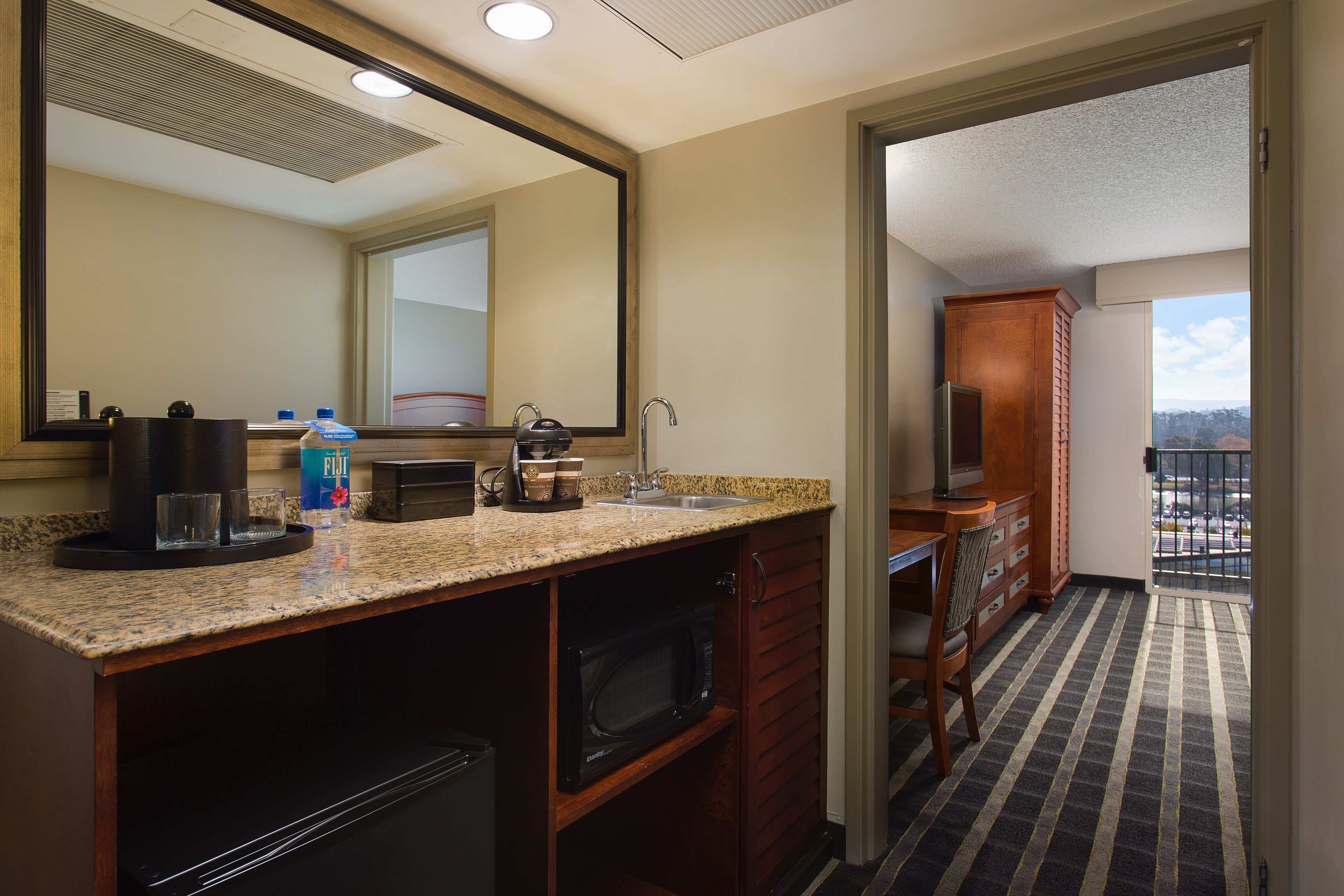 A hotel bathroom with a sink, mirror, and a view of the balcony.