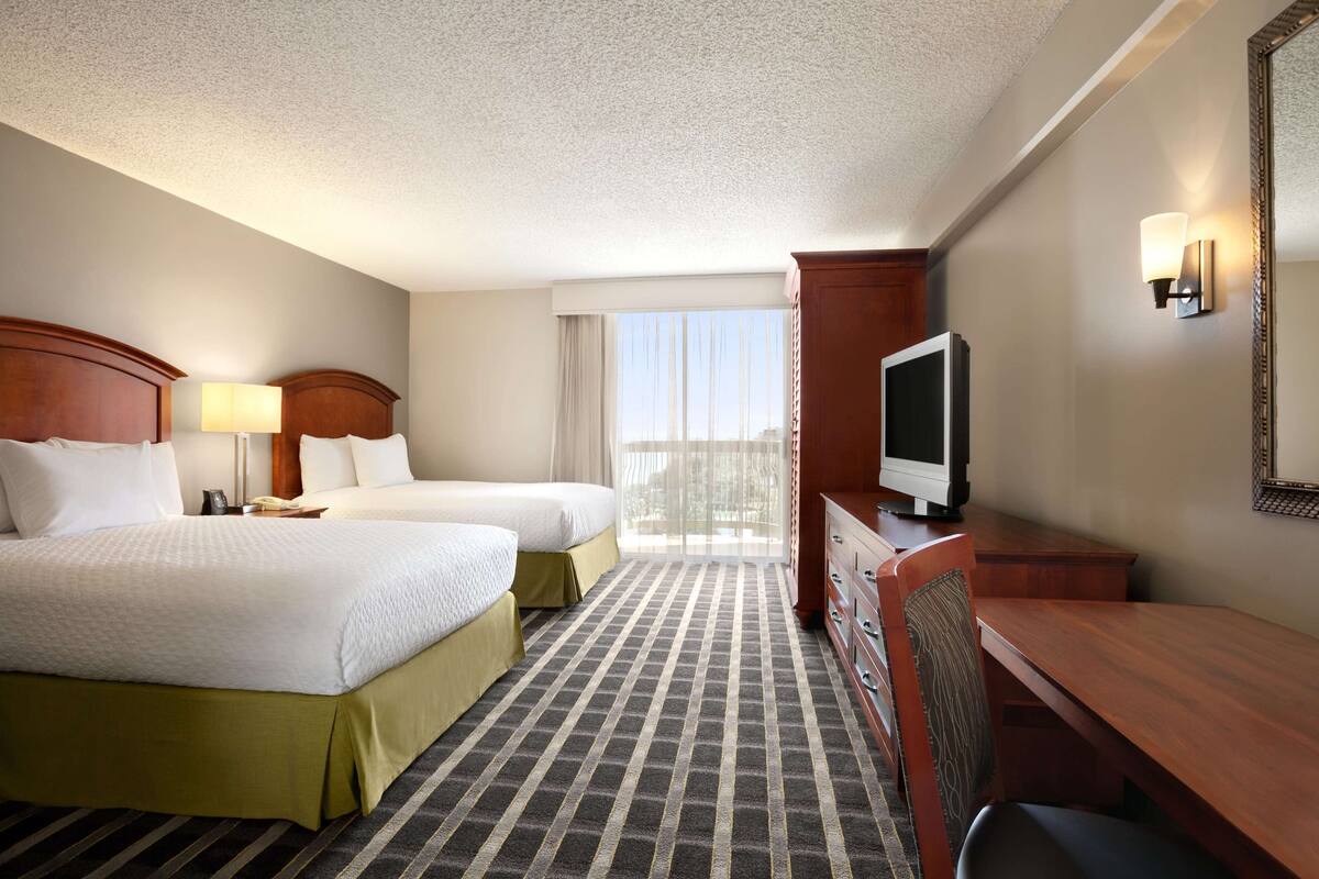 A hotel room with two beds, a desk, a television, and a window with a view.