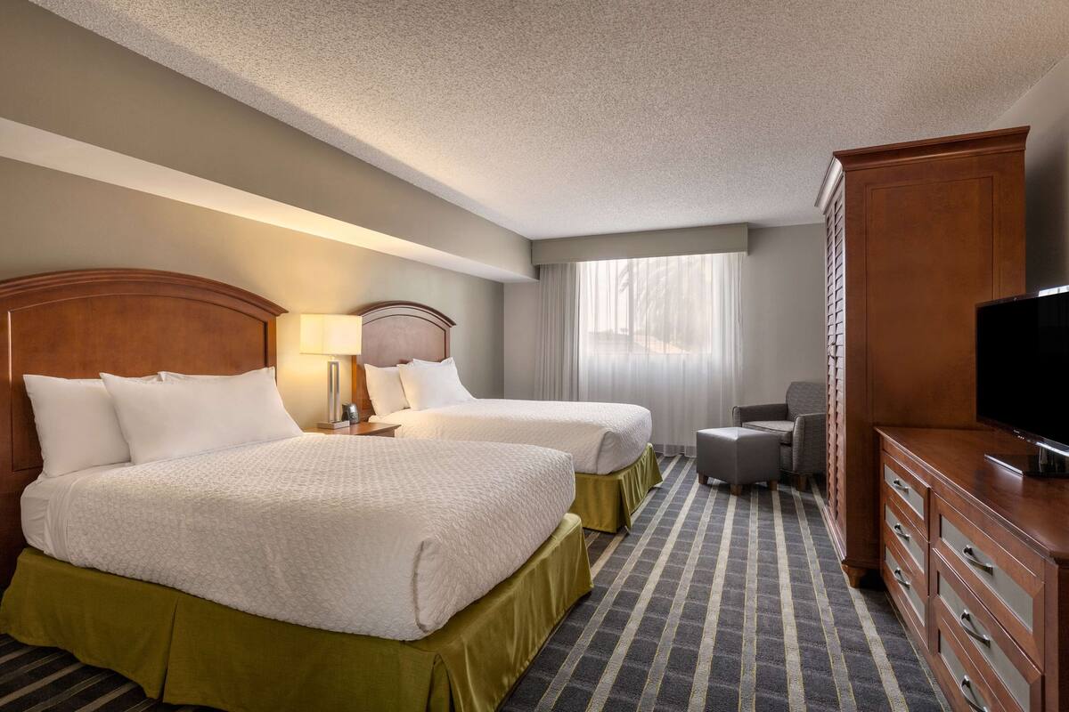 A hotel room with two beds, a TV, a desk, and a chair.