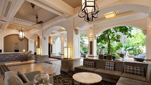 A spacious lobby with a reception desk, seating areas, and large windows offering views of greenery.