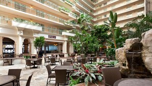 A multi-level hotel atrium with outdoor seating, a waterfall feature, and a restaurant named "GRILLE ONE."
