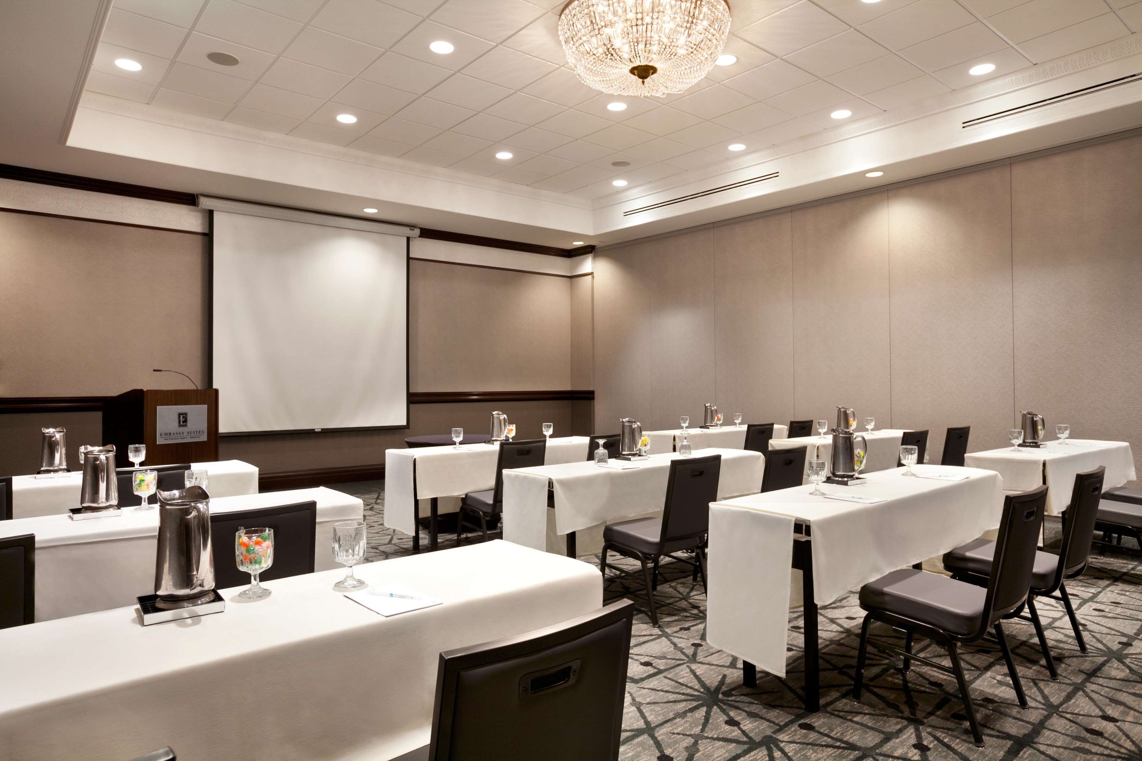 A conference room with multiple tables, chairs, and a projector screen.