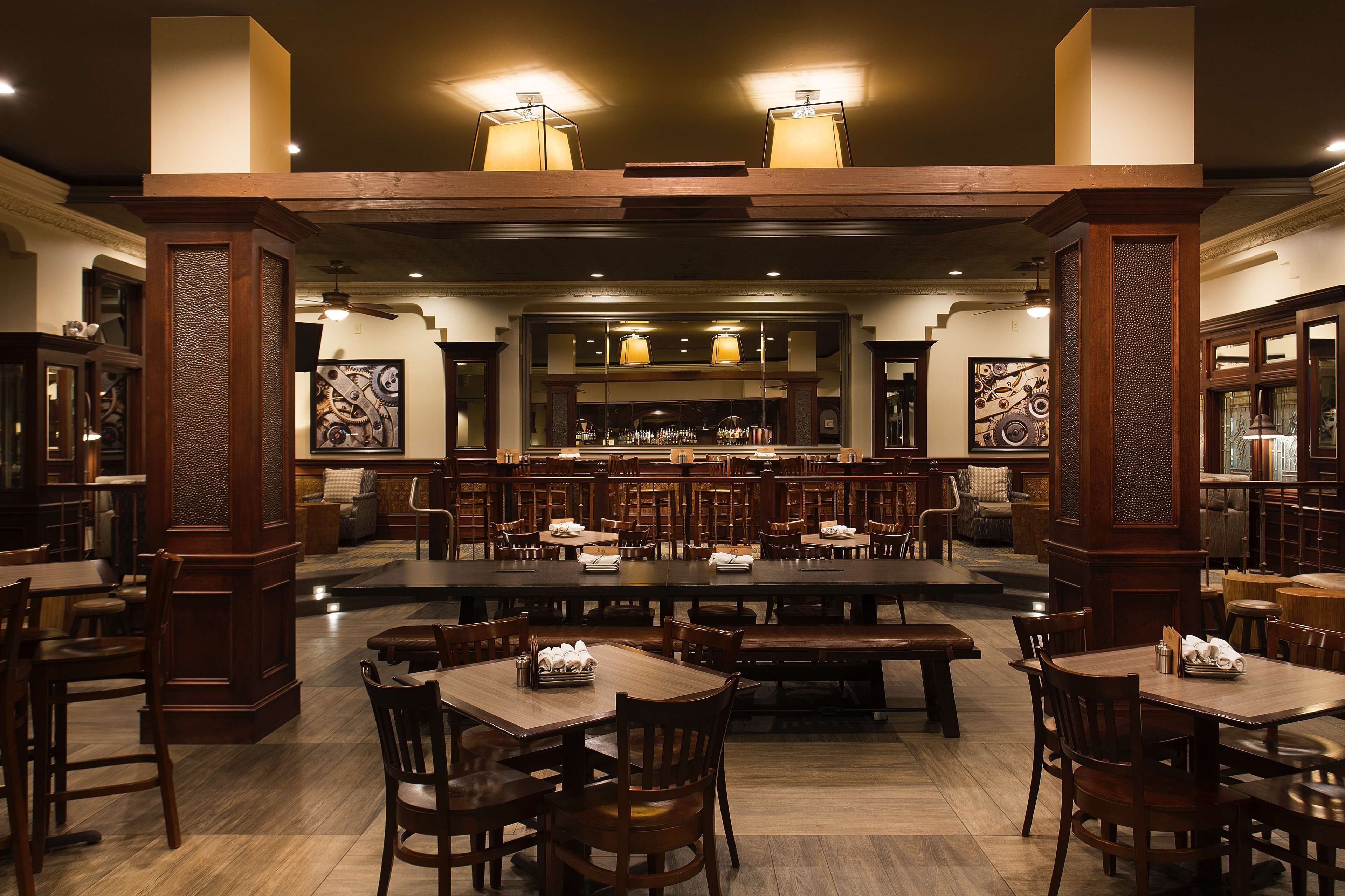 A spacious restaurant with high wooden tables and chairs, a central bar area, and decorative wall art.