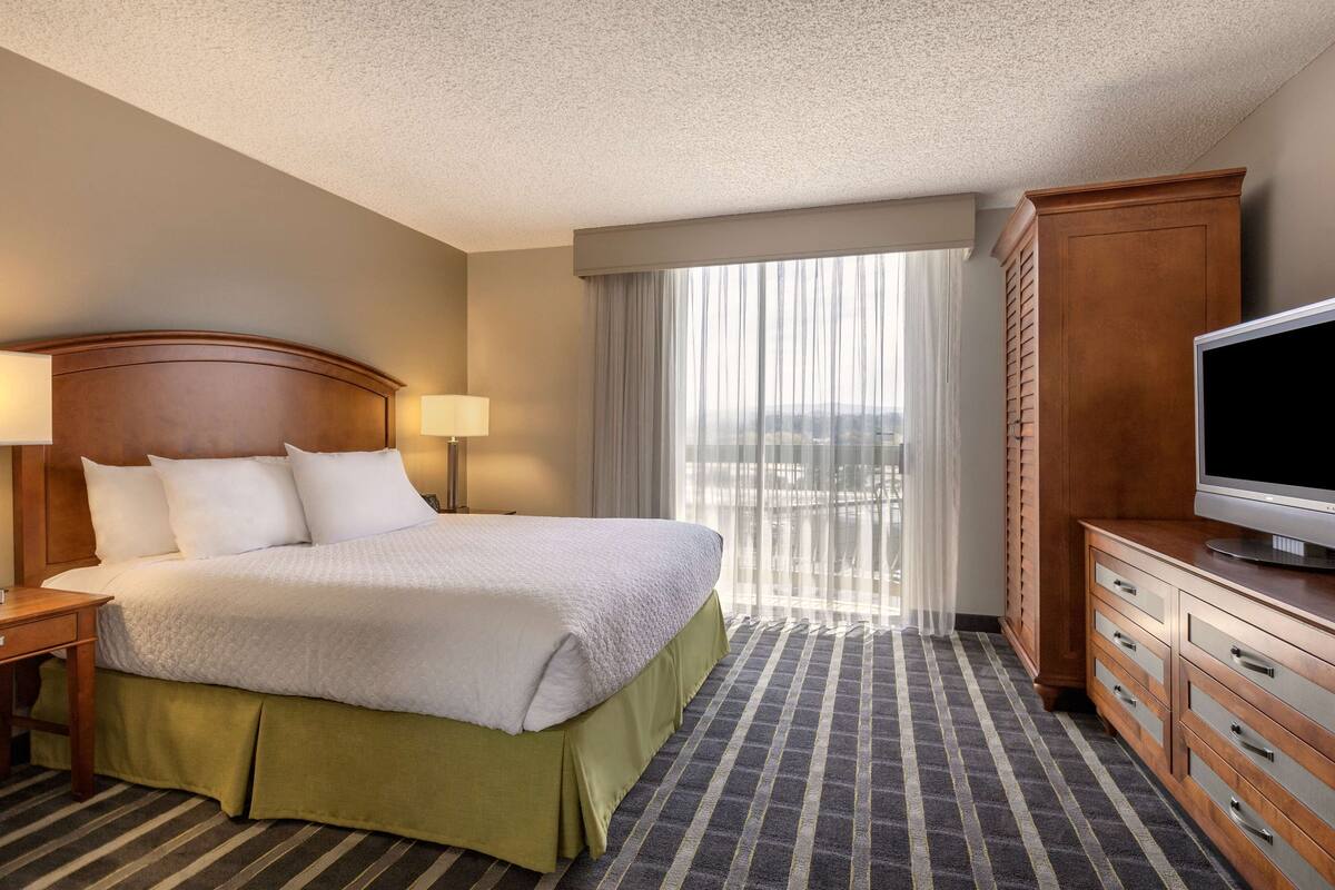A hotel room with a bed, a television, a desk, and a window with curtains.