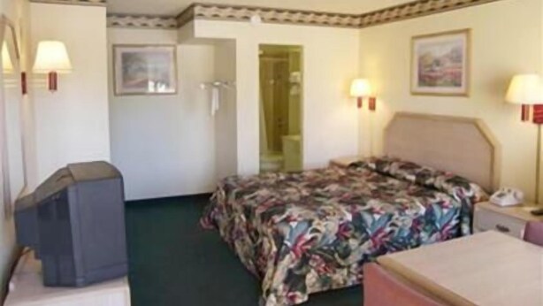 Ett hotellrum med en säng, ett skrivbord, en stol, en tv och en dörr som leder till badrummet.