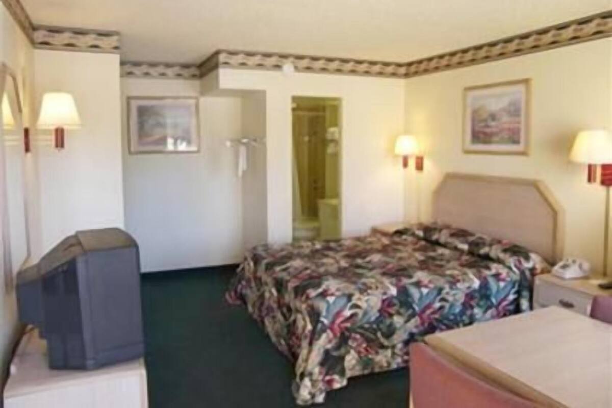 Une chambre d’hôtel équipée d’un lit, d’un bureau, d’une chaise, d’une télévision et d’une porte donnant accès à la salle de bain.