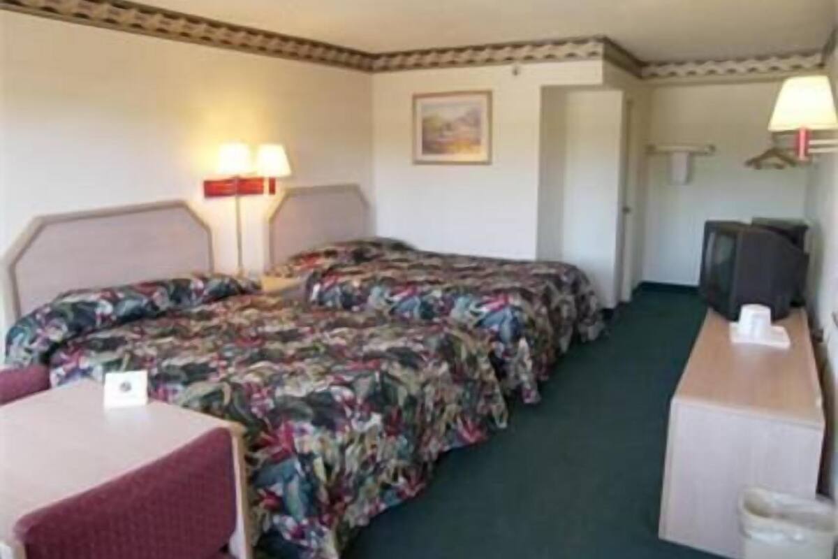 Une chambre d’hôtel avec deux lits, un bureau, une chaise, une télévision et une poubelle.