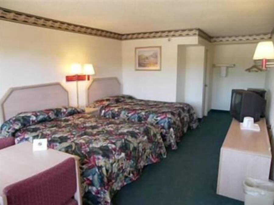 A hotel room with two beds, a desk, a chair, a television, and a trash bin.