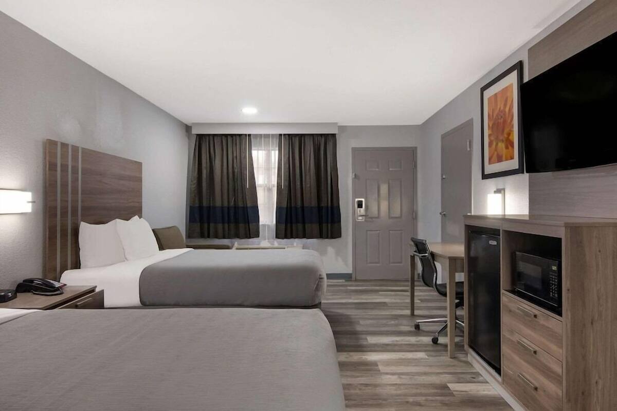 A hotel room with two beds, a desk, a television, and a microwave.