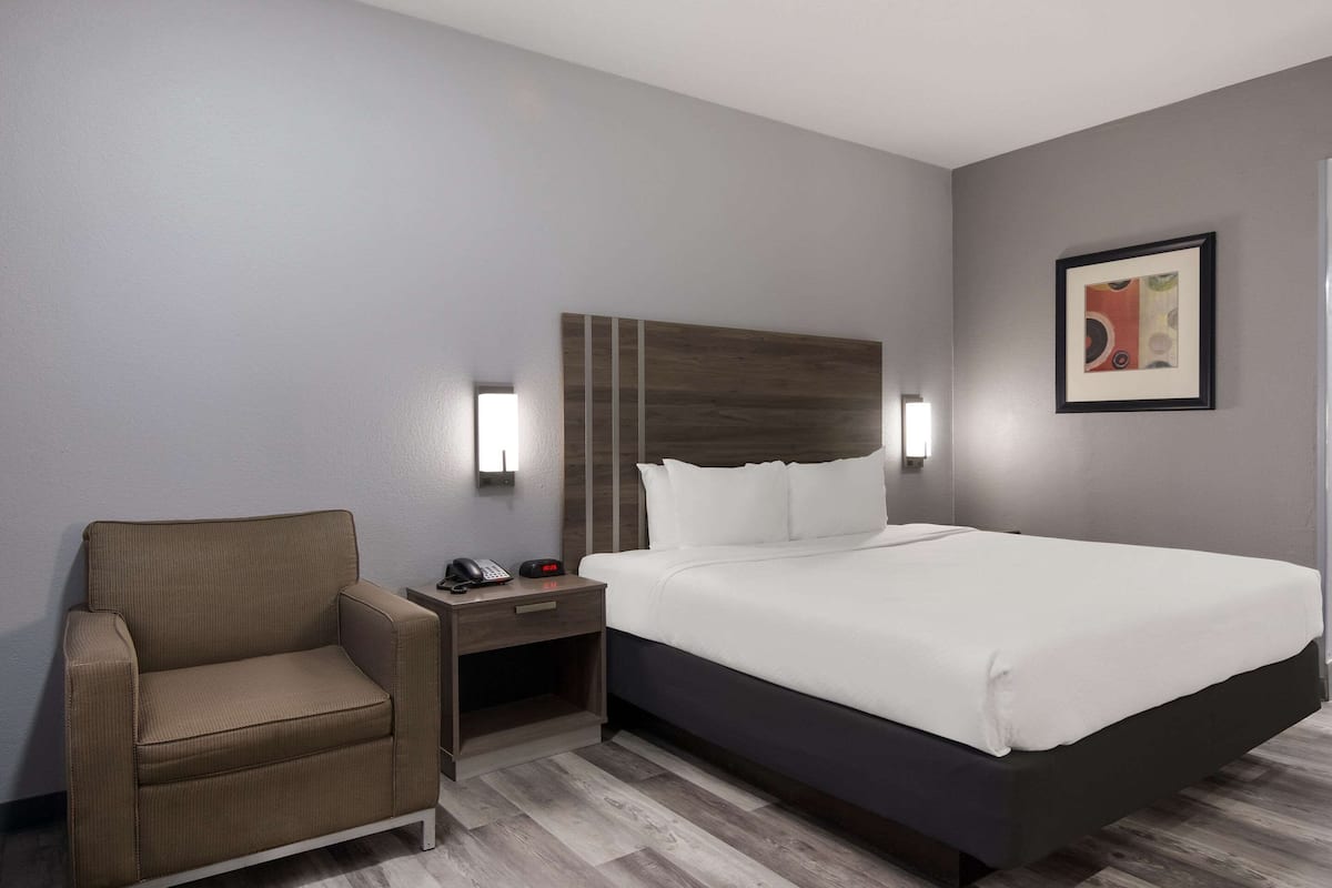 A hotel room with a bed, a chair, a nightstand, and a wall-mounted light.