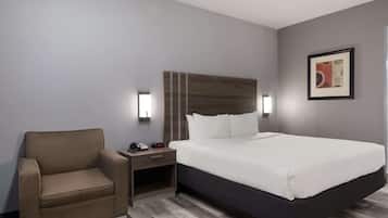 Quarto de hotel com cama, uma cadeira, mesa de cabeceira e luminária na parede.