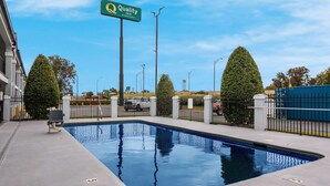 A swimming pool with a chair, a Quality Inn sign, and a fenced area with trees. - Quality Inn near Casinos and Convention Center (Bossier City)