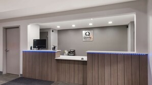 A reception desk with a 'Quality by Choice Hotels' sign, a flat-screen TV, and a blue LED light strip. - Quality Inn near Casinos and Convention Center (Bossier City)