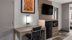 A modern hotel room with a wooden desk, a black office chair, a flat-screen TV mounted on the wall, and a built-in refrigerator. - Quality Inn near Casinos and Convention Center (Bossier City)