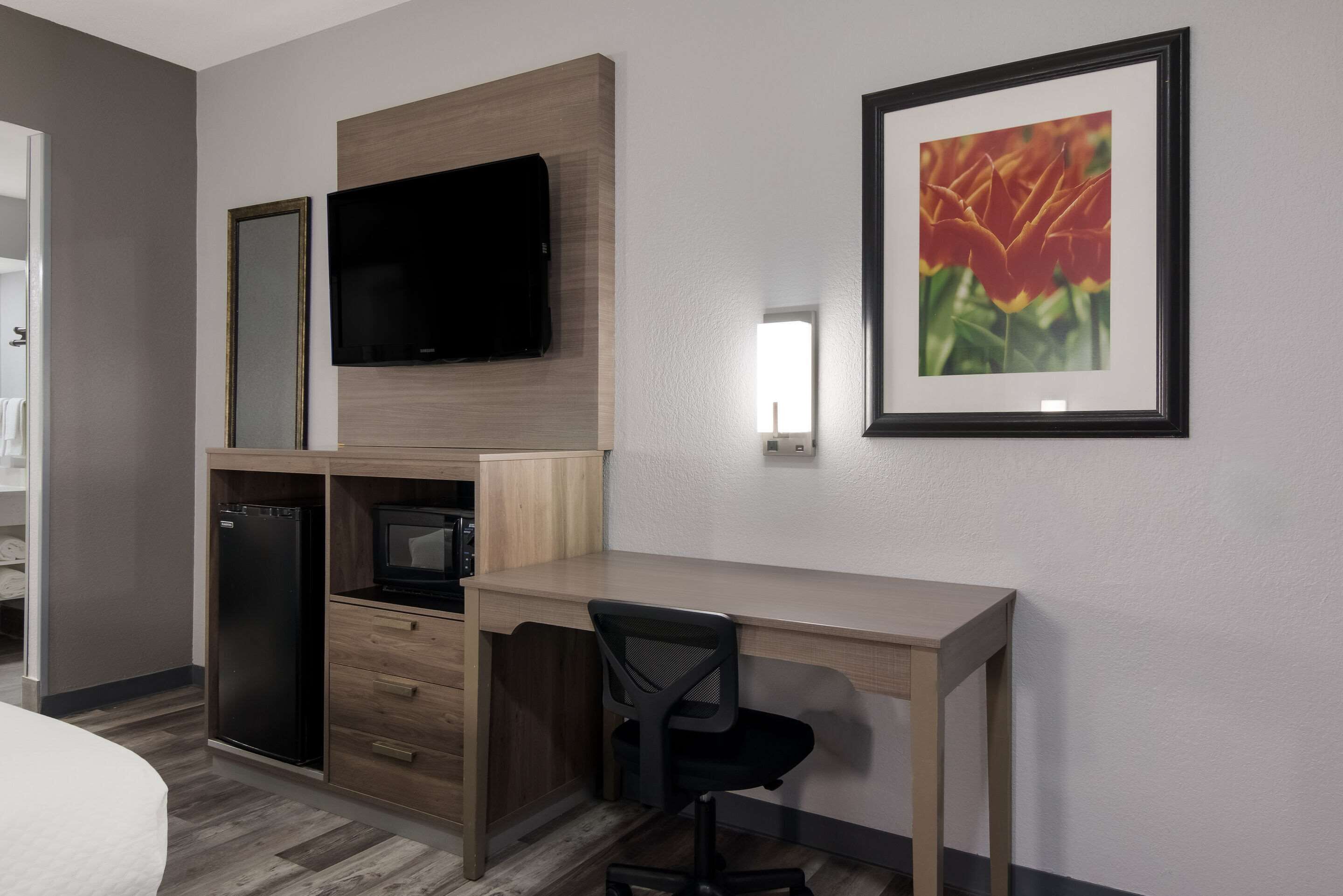 Une chambre d’hôtel comprenant un lit, un bureau avec une chaise, une télévision, un réfrigérateur, un four à micro-ondes et un tableau encadré au mur.