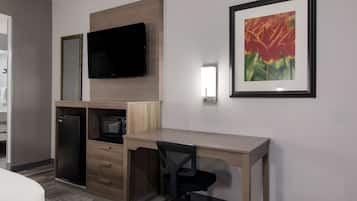 Une chambre d’hôtel comprenant un lit, un bureau avec une chaise, une télévision, un réfrigérateur, un four à micro-ondes et un tableau encadré au mur.