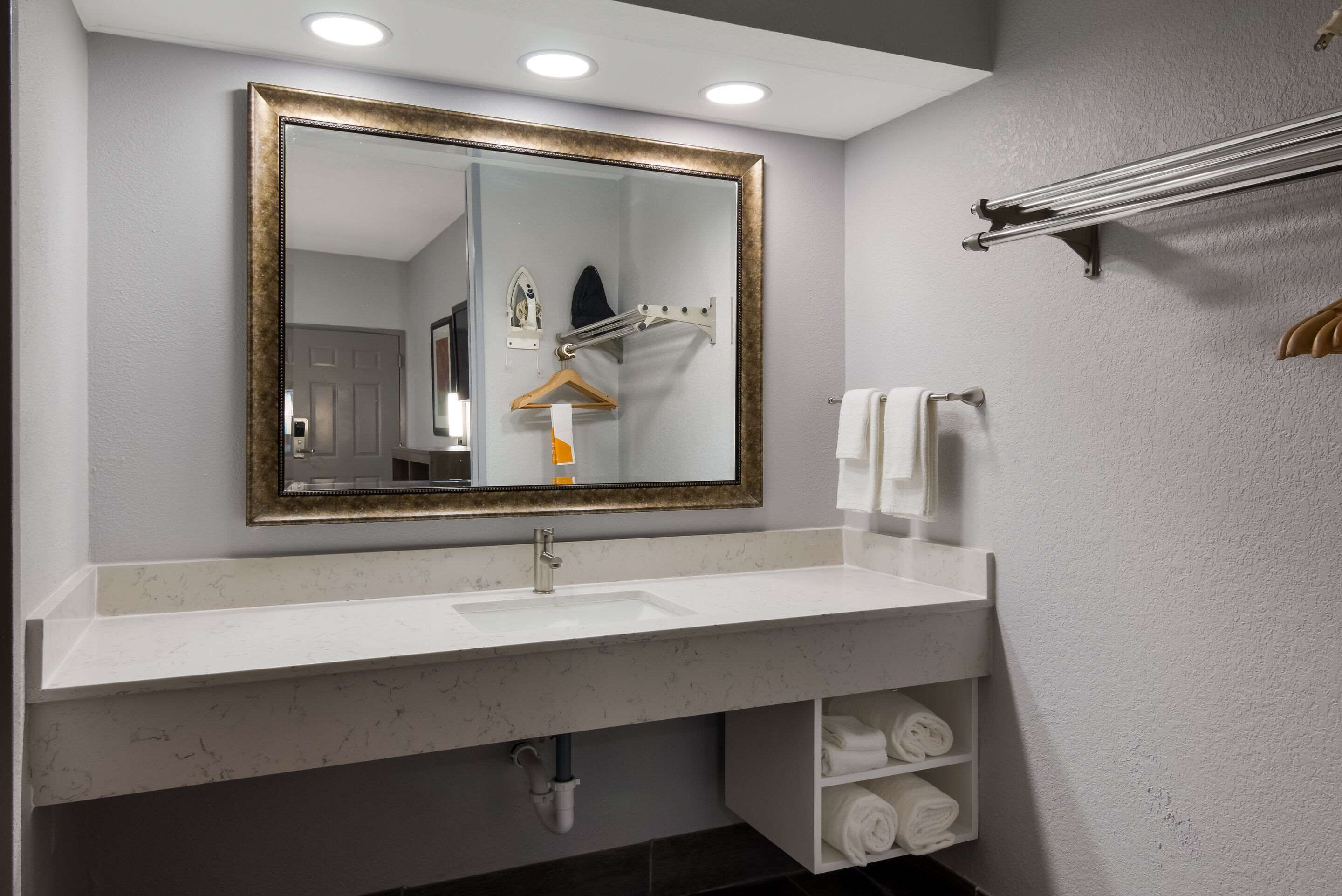 Un baño con un lavamanos blanco, un espejo grande con marco dorado, un perchero y un estante con toallas.
