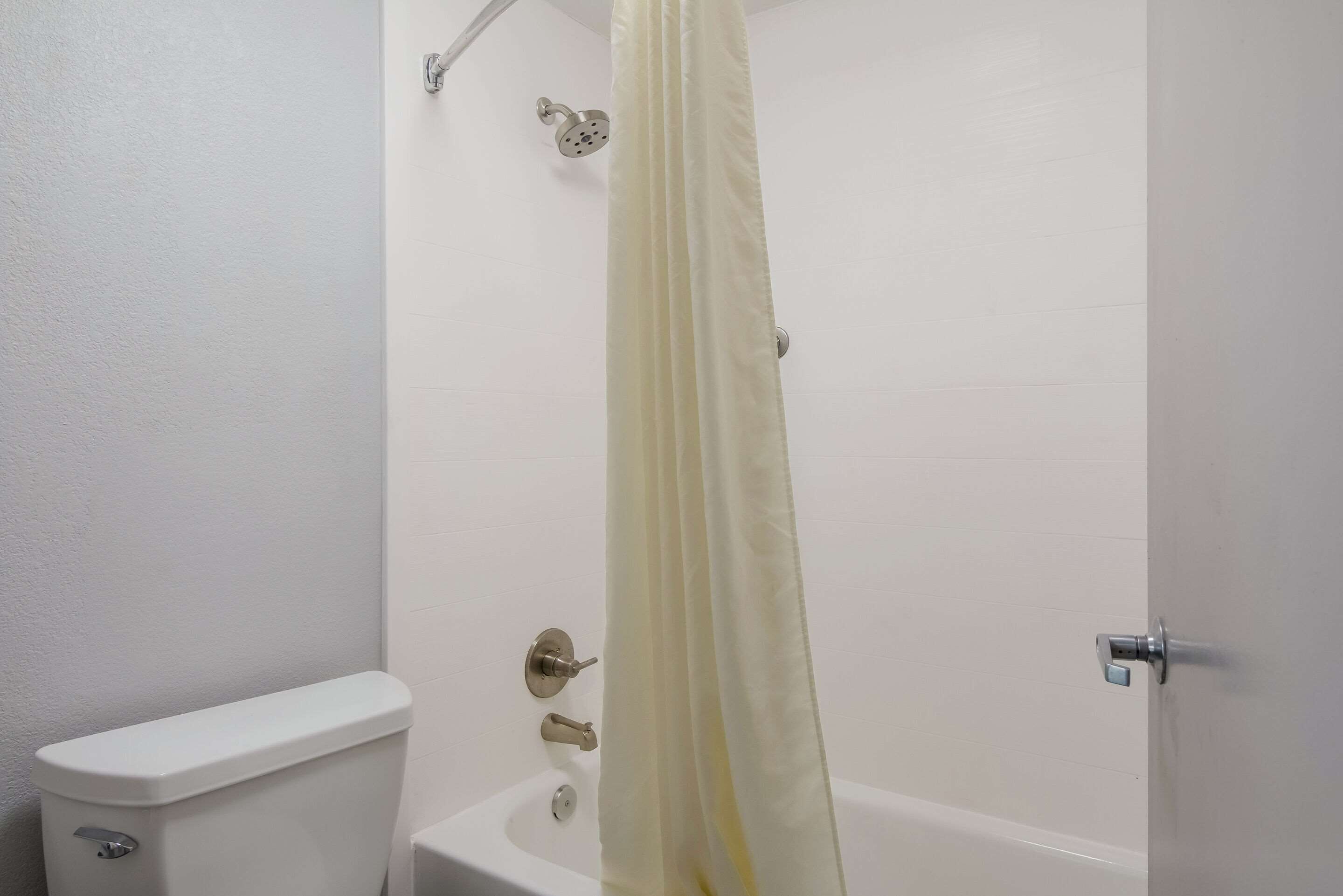 A bathroom with a toilet, a shower with a curtain, and a bathtub.