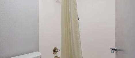 A bathroom with a toilet, a shower with a curtain, and a bathtub.