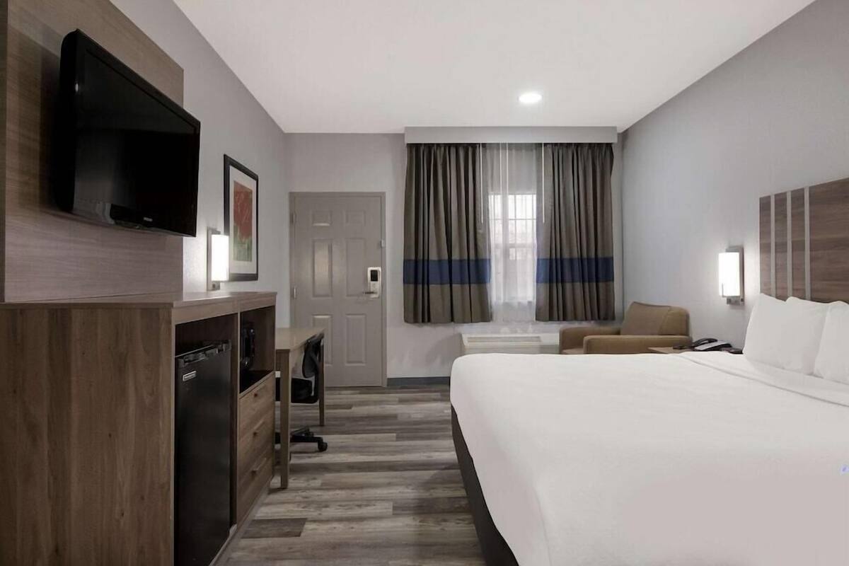 A hotel room with a bed, a desk, a television, and a window with curtains.
