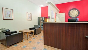 Een receptiegedeelte met een houten receptiebalie, een bank, een bijzettafeltje en een klok aan de muur.