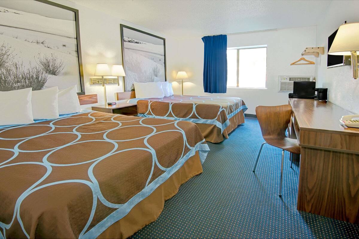 Une chambre d’hôtel avec deux lits, un bureau, une chaise, une télévision et une fenêtre avec un rideau bleu.
