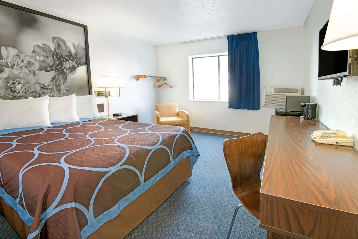 Une chambre d’hôtel avec un grand lit, un bureau, une chaise, une télévision et une fenêtre avec des rideaux.