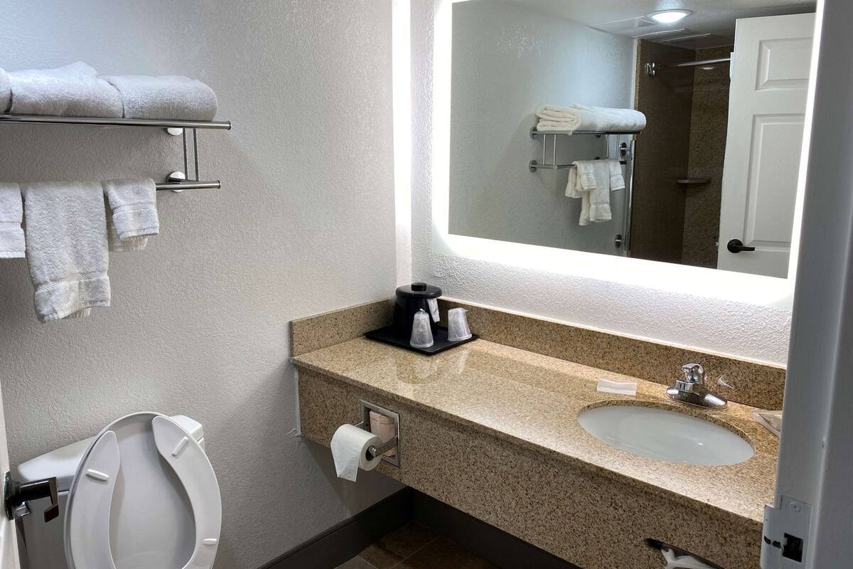 A bathroom with a toilet, sink, towel rack, and a mirror with a light above it.