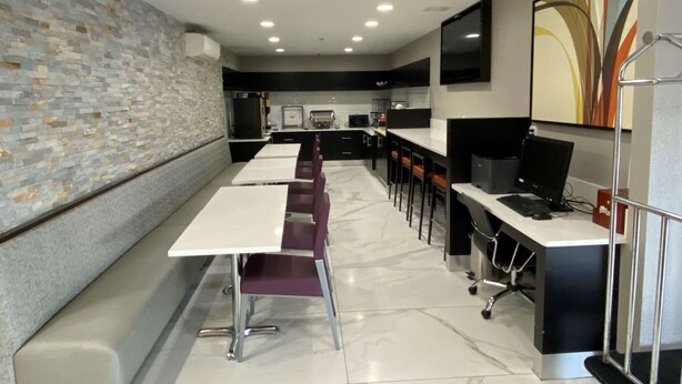 A modern kitchen with white countertops, black appliances, and a stone backsplash. There are multiple bar stools and a long dining table. - Best Western Kennesaw (Kennesaw)