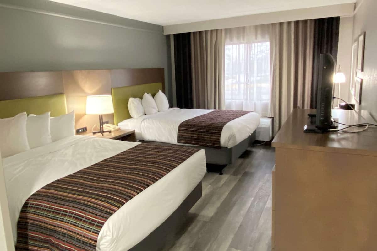 A hotel room with two beds, a desk, a TV, and a window with curtains.