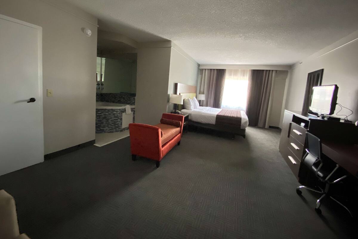 A hotel room with a bed, a desk, a chair, a small sofa, and a bathroom visible through an open door.