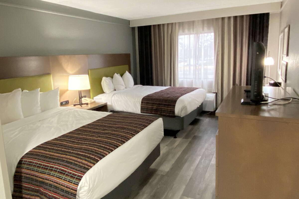 A hotel room with two beds, a desk, a lamp, and a TV.