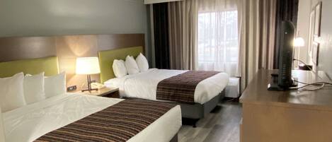 Quarto de hotel com duas camas, uma escrivaninha, uma luminária e uma televisão.