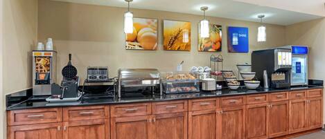 A buffet setup with various food stations, including a waffle maker, a coffee machine, and a rice cooker.