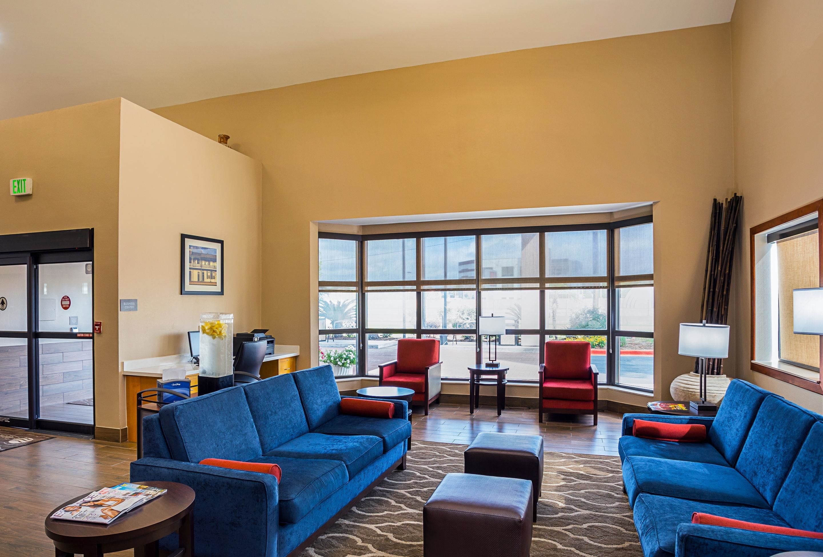 A hotel lobby with blue sofas, red chairs, a reception desk, and large windows offering a view of the outside. - Comfort Inn University Area (Baton Rouge)