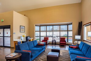 Un hall d’hôtel avec des canapés bleus, des fauteuils rouges, un comptoir d’accueil et de grandes fenêtres donnant sur l’extérieur.