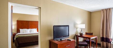 Une chambre d’hôtel avec un lit, un téléviseur posé sur une commode en bois, un bureau avec une lampe et une vue sur le couloir.