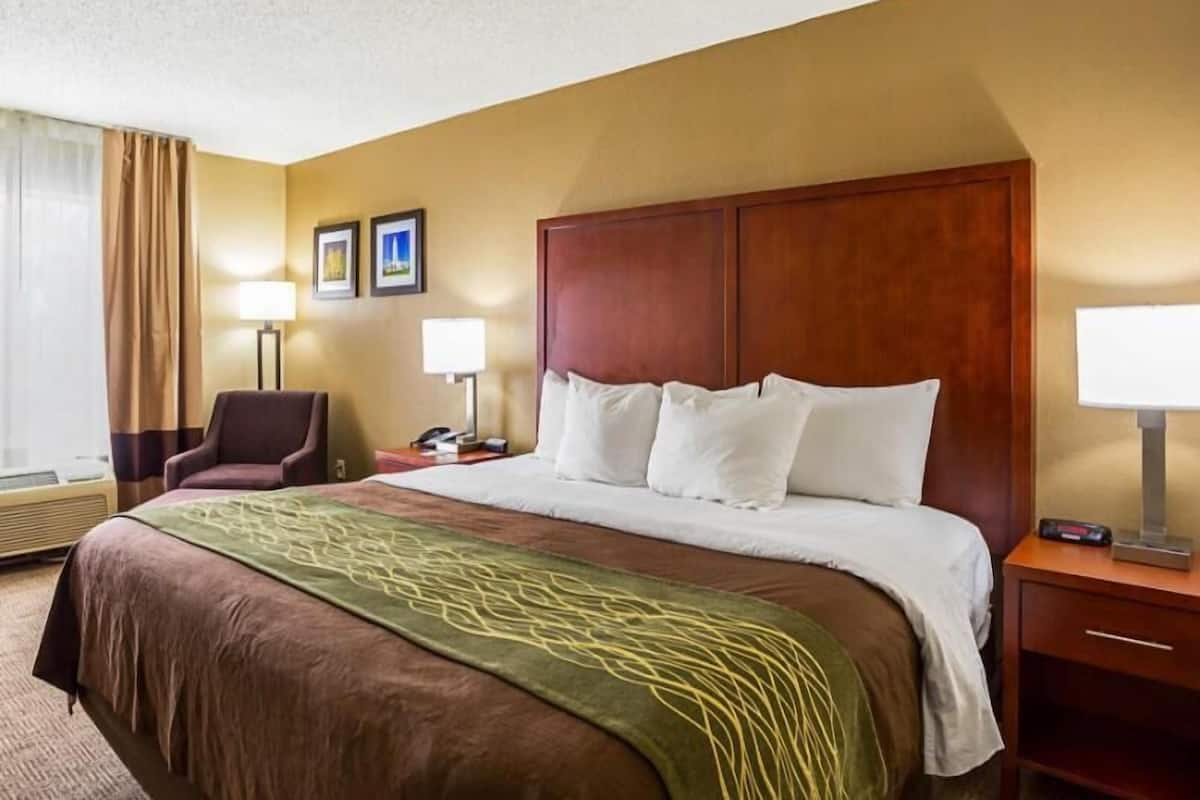 A hotel room with a large bed, a chair, two bedside lamps, and a window with curtains.