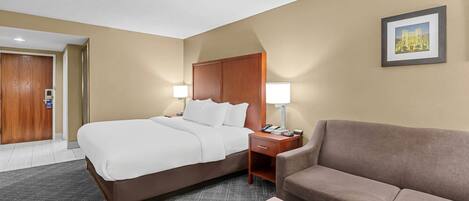 A hotel room with a large bed, a sofa, a nightstand with a lamp, and a framed picture on the wall.