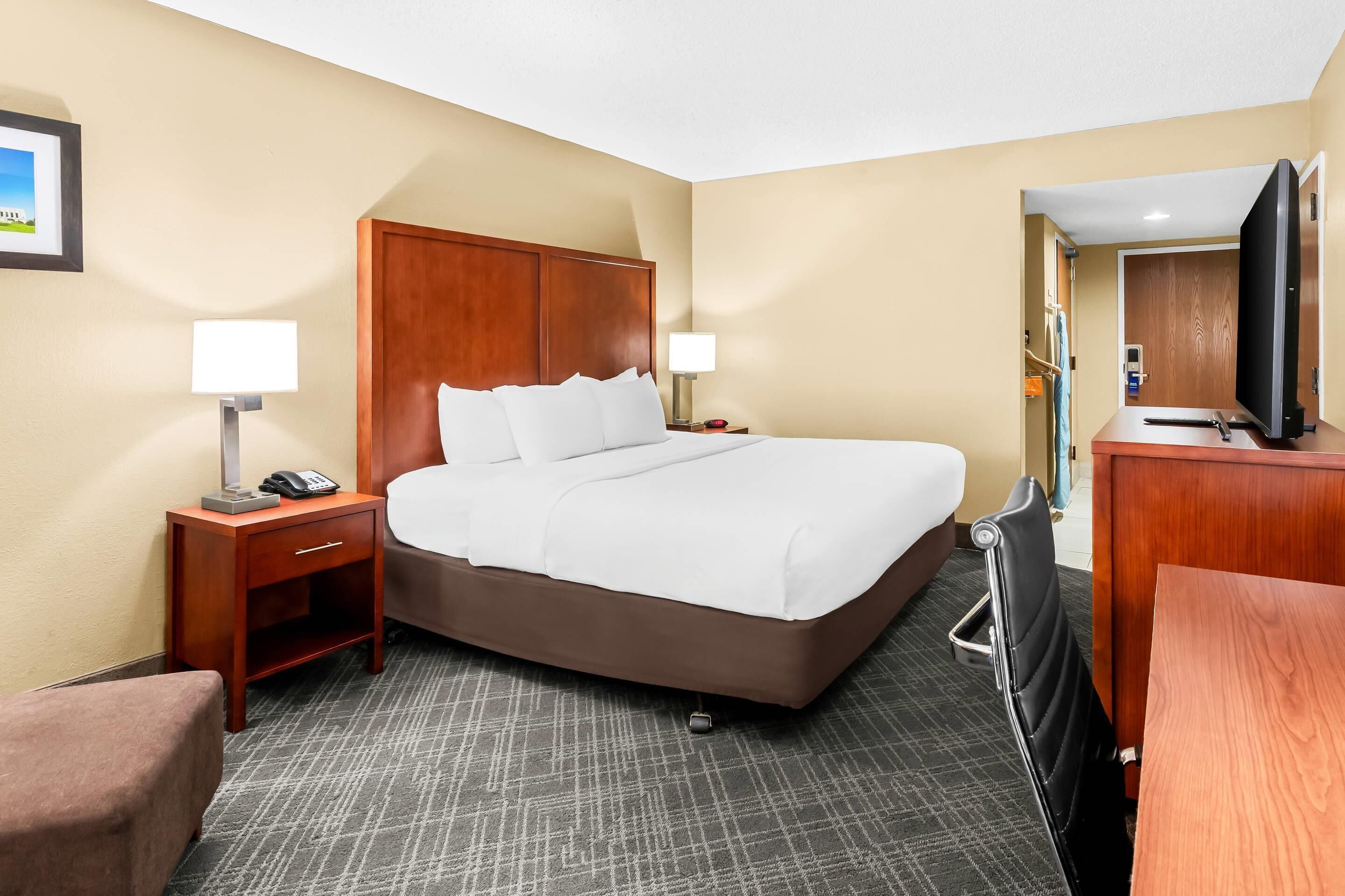 A hotel room with a large bed, a desk, a chair, a TV, and a small table.
