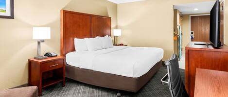 A hotel room with a large bed, a desk, a chair, a TV, and a small table.