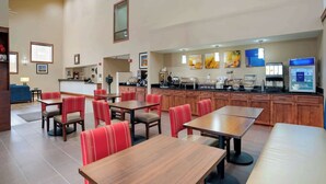 A hotel dining area with multiple tables and chairs, a kitchen area with a buffet, and a reception desk. - Comfort Inn University Area (Baton Rouge)