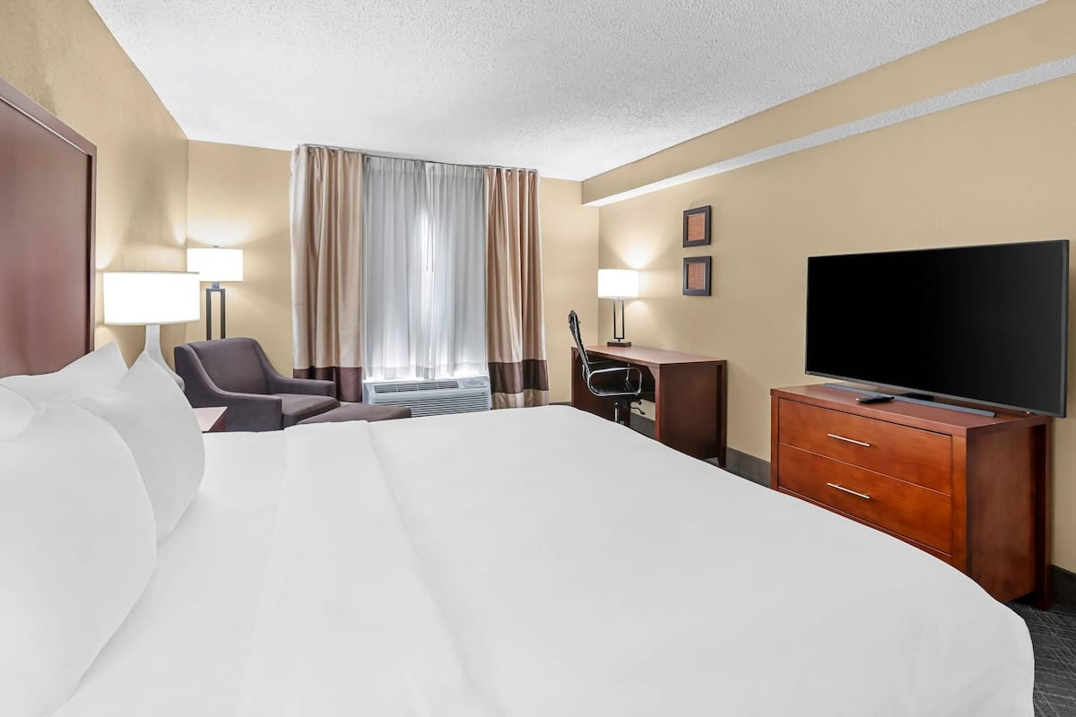 A hotel room with a large bed, a desk with a chair, a television, and a window with curtains.