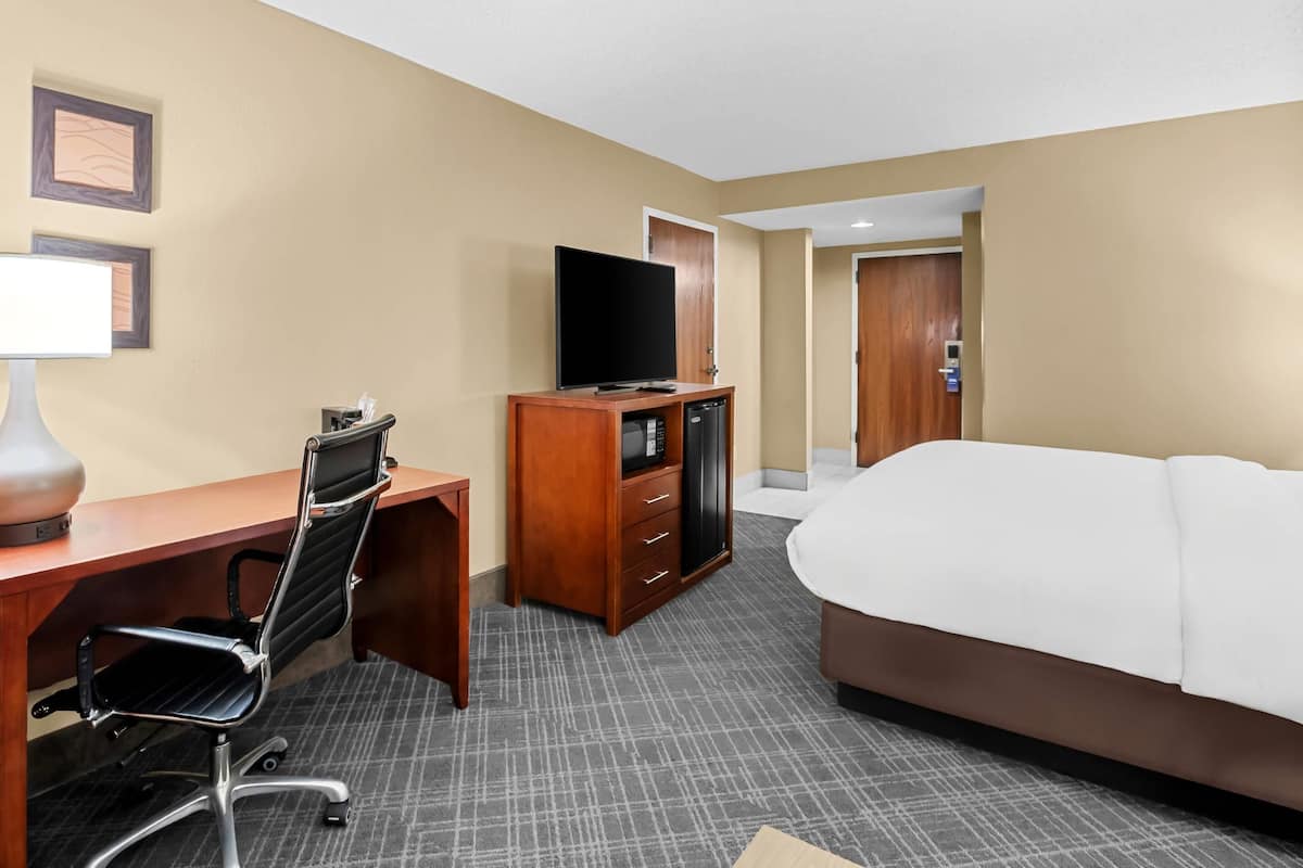 A hotel room with a bed, a desk with a chair, a television, and a minibar.
