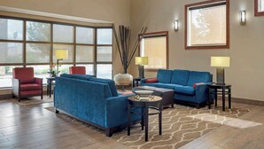 A spacious living room with a large window, two sofas, a coffee table, and a red armchair. - Comfort Inn University Area (Baton Rouge)