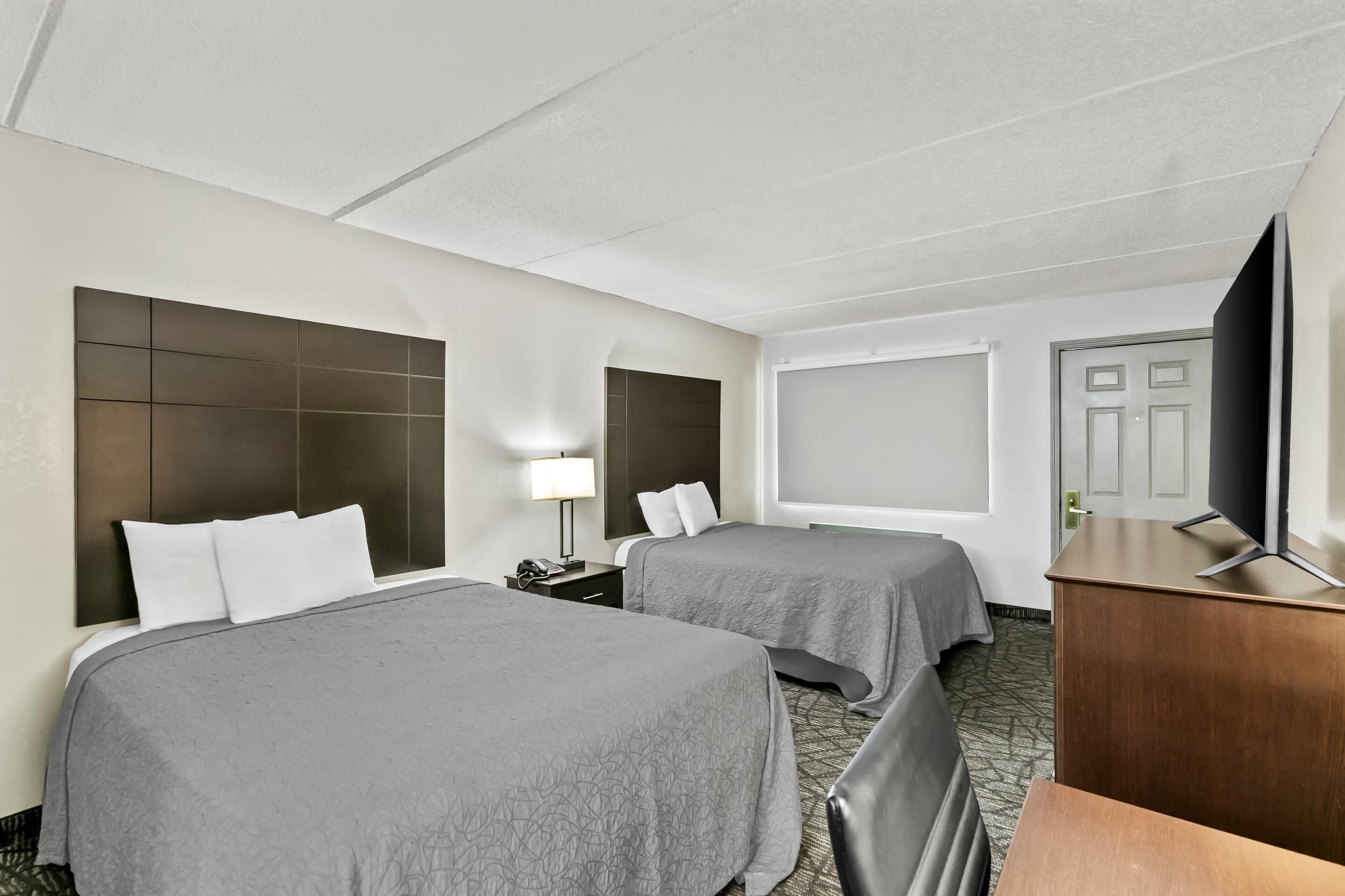 Habitación de hotel con dos camas, televisión, escritorio y un ventanal grande.