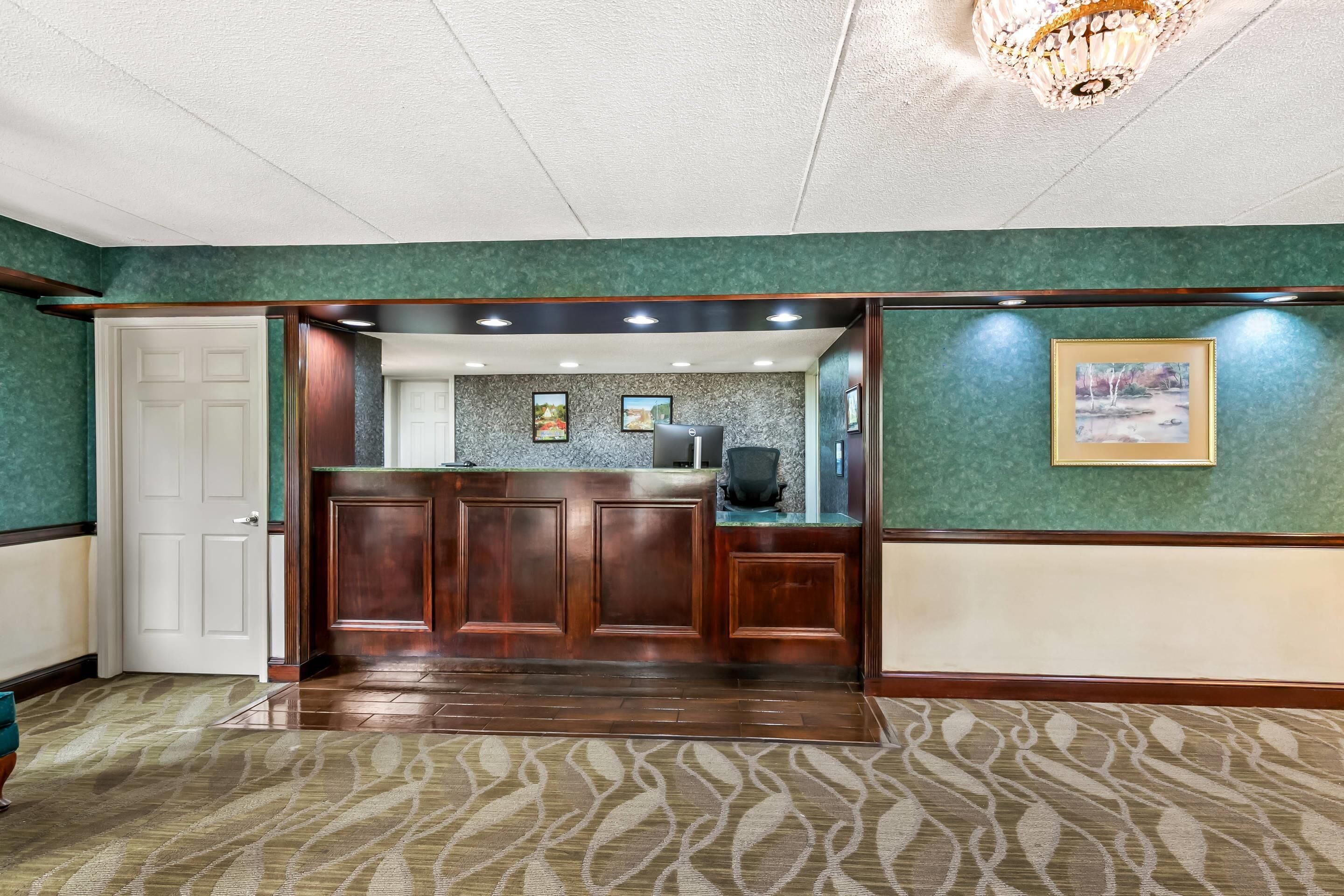 A reception area with a wooden reception desk, a white door, and a green wall with framed pictures.