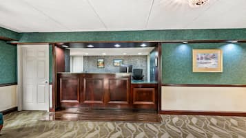 A reception area with a wooden reception desk, a white door, and a green wall with framed pictures.